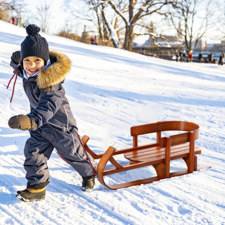 kid playing in the snow with wooden sled